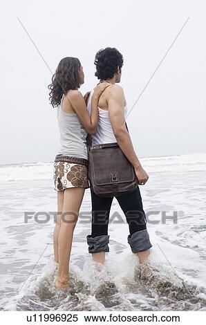 Stock Photography - Side profile of a young couple standing on the beach. Fotosearch