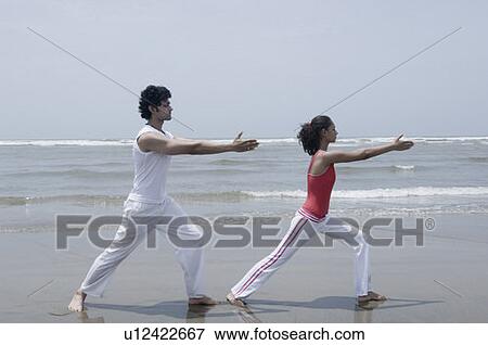 Stock Photo - Side profile of a young couple exercising on the beach. Fotosearch