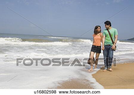 Stock Photo - Young couple walking on the beach with holding hands. Fotosearch