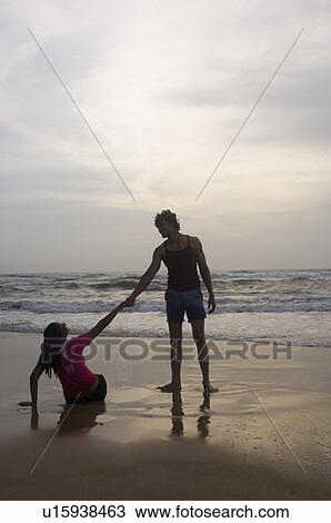 Stock Image - Young man holding a young woman's hand on the beach. Fotosearch