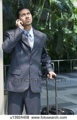 Businessman talking on a mobile phone and holding his luggage View Large Photo Image Stock Photo - Businessman talking on a mobile phone and holding his luggage. Fotosearch