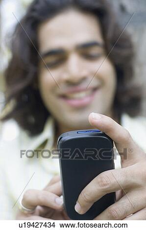 Close-up of a young man text messaging with a mobile phone View Large Photo Image Picture - Close-up of a young man text messaging with a mobile phone. Fotosearch