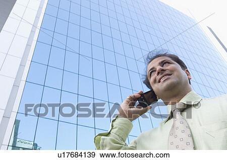 Stock Photo - Low angle view of a businessman talking on a mobile phone and smiling. Fotosearch