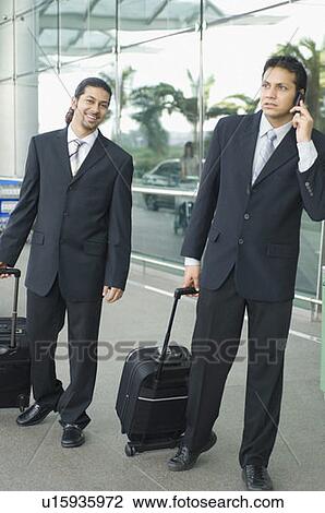 Stock Image - Two businessmen standing at an airport and waiting. Fotosearch