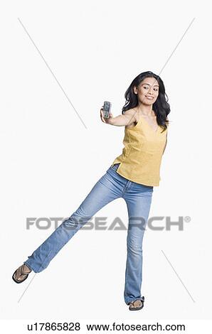 Stock Photo - Young woman standing on her one leg and taking a photograph of herself with a mobile phone. Fotosearch