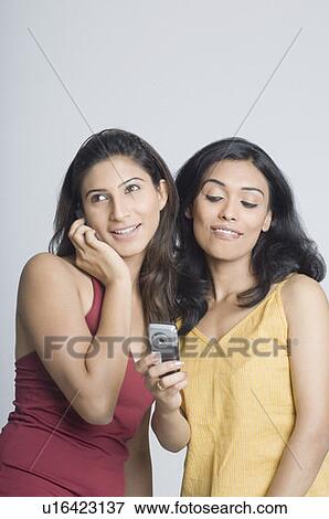 Stock Photo - Young woman talking on a mobile phone and another young woman reading a message. Fotosearch