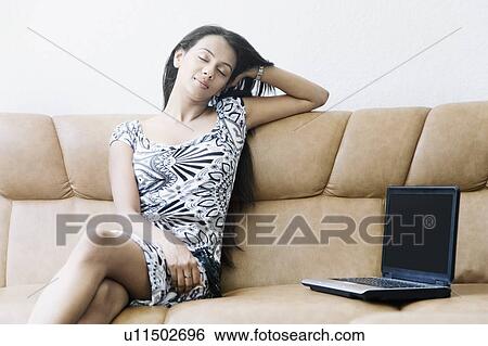 Stock Photograph - Young woman sitting on a couch with a laptop beside her. Fotosearch
