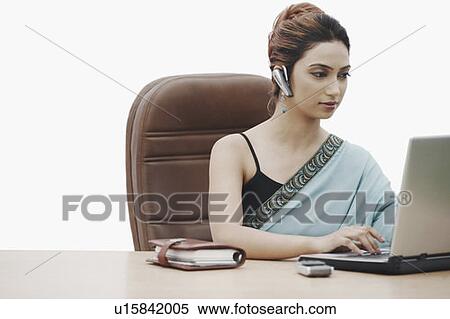 Businesswoman working on a laptop wearing a hands free device View Large Photo Image Stock Photography - Businesswoman working on a laptop wearing a hands free device. Fotosearch