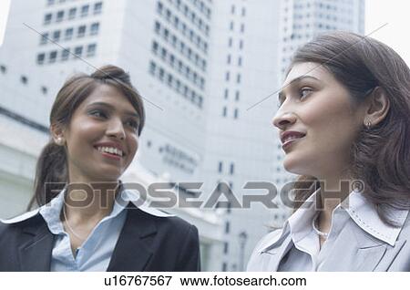 Close-up of two businesswomen looking at each other and smiling, Singapore View Large Photo Image Stock Photo - Close-up of two businesswomen looking at each other and smiling, Singapore. Fotosearch