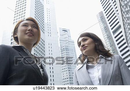 Stock Image - Low angle view of two businesswomen standing, Singapore. Fotosearch