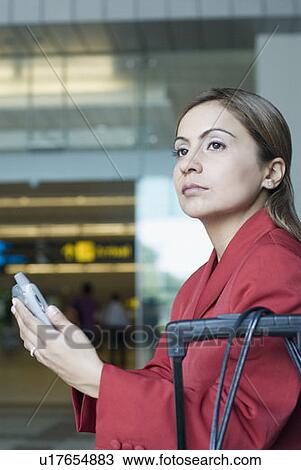 Stock Image - Side profile of a businesswoman holding a mobile phone and waiting at an airport. Fotosearch