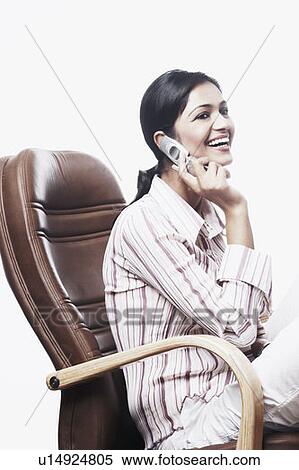 Stock Photography - Side profile of a businesswoman sitting on a chair and talking on a mobile phone. Fotosearch