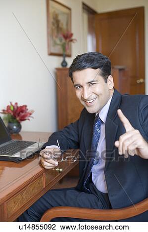 Stock Image - Portrait of a businessman sitting in front of a laptop and smiling. Fotosearch