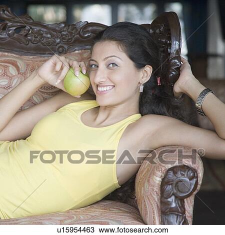 Stock Image - Portrait of a young woman holding a granny smith apple and smiling. Fotosearch