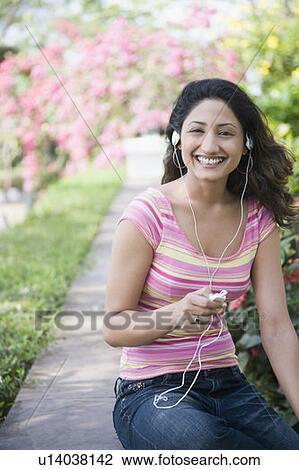 Stock Image - Portrait of a young woman listening to music with an Mp3 player and smiling. Fotosearch