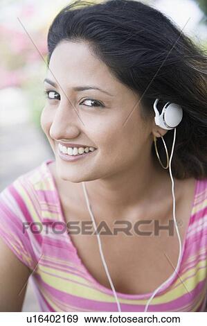Stock Photo - Portrait of a young woman listening to music with an Mp3 player and smiling. Fotosearch