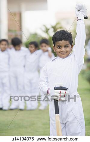 Stock Photography - Portrait of a cricket player standing in a cricket field with other cricket players standing in the background. Fotosearch