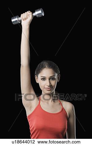 Stock Image - Portrait of a young woman exercising with a dumbbell. Fotosearch