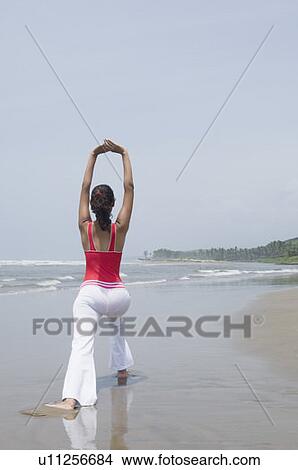 Rear view of a young woman exercising on the beach View Large Photo Image Picture - Rear view of a young woman exercising on the beach. Fotosearch