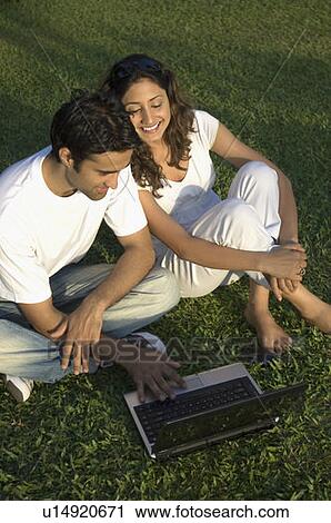 Stock Image - High angle view of a young couple using a laptop in a garden. Fotosearch