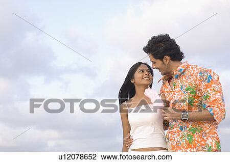 Stock Image - Low angle view of a young man offering a cotton candy to a young woman. Fotosearch