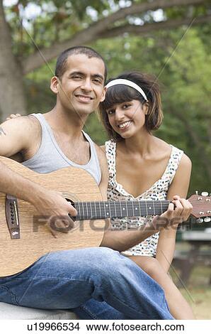 Picture - Portrait of a young man sitting with his girlfriend and playing a guitar. Fotosearch