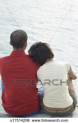 Rear view of a young couple sitting on the beach View Large Photo Image Stock Photo - Rear view of a young couple sitting on the beach. Fotosearch