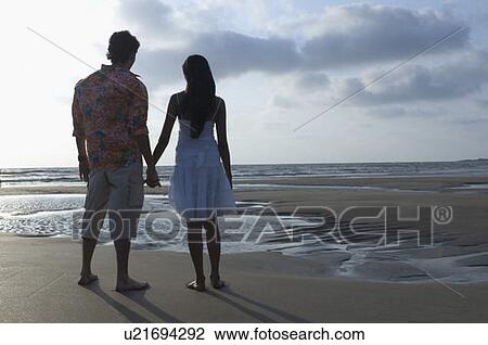 Rear view of a young couple with holding hands and standing on the beach View Large Photo Image Stock Image - Rear view of a young couple with holding hands and standing on the beach. Fotosearch