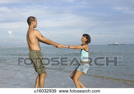 Stock Photo - Side profile of a young couple holding hands on the beach. Fotosearch