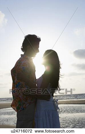 Stock Image - Side profile of a young couple embracing each other. Fotosearch