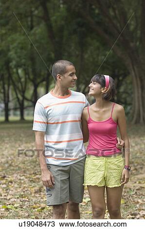 Stock Image - Young couple walking in a park and looking at each other . Fotosearch