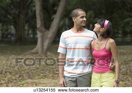 Stock Photography - Young couple walking in a park and looking at each other . Fotosearch