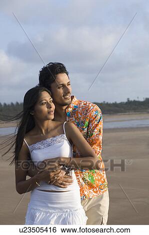 Young man embracing a young woman from behind on the beach View Large Photo Image Stock Photograph - Young man embracing a young woman from behind on the beach. Fotosearch