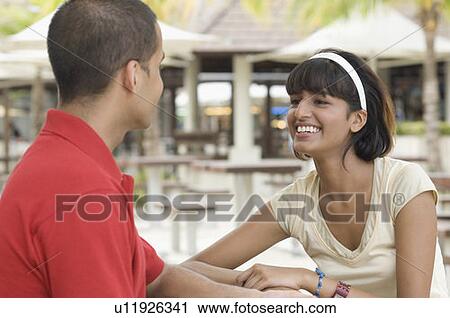 Stock Image - Young woman sitting with a young man in a restaurant and smiling. Fotosearch