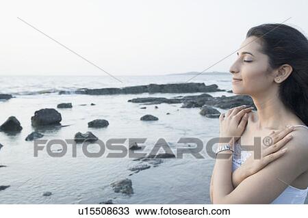 Stock Image - Close-up of a young woman hugging herself on the coast. Fotosearch