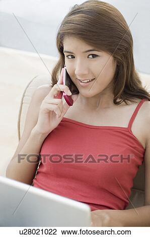 Close-up of a young woman talking on a mobile phone with a laptop on her lap View Large Photo Image Stock Image - Close-up of a young woman talking on a mobile phone with a laptop on her lap. Fotosearch