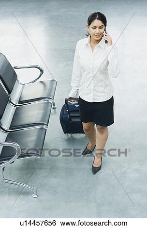 High angle view of a businesswoman holding her luggage and talking on a mobile phone at an airport View Large Photo Image Stock Photograph - High angle view of a businesswoman holding her luggage and talking on a mobile phone at an airport. Fotosearch