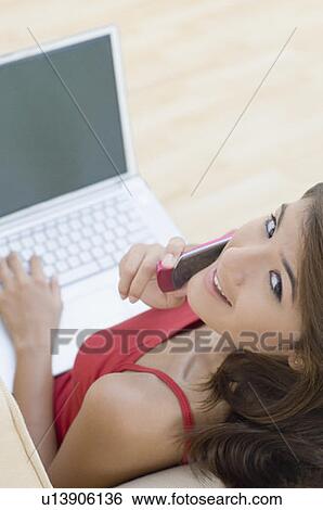 High angle view of a young woman using a laptop and talking on a mobile phone View Large Photo Image Stock Photograph - High angle view of a young woman using a laptop and talking on a mobile phone. Fotosearch
