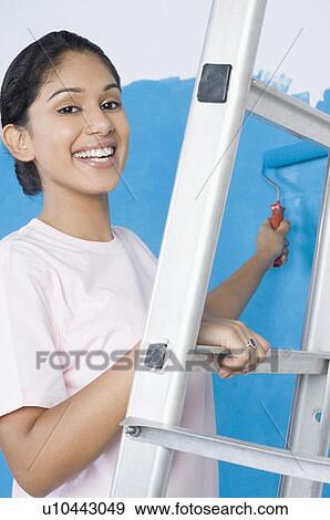 Portrait of a young woman painting a wall with a paint roller View Large Photo Image Stock Photo - Portrait of a young woman painting a wall with a paint roller. Fotosearch