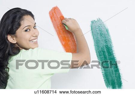 Picture - Portrait of a young woman painting the Indian flag on a wall and smiling. Fotosearch