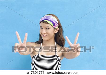 Portrait of a young woman showing peace sign and smiling View Large Photo Image Stock Image - Portrait of a young woman showing peace sign and smiling. Fotosearch
