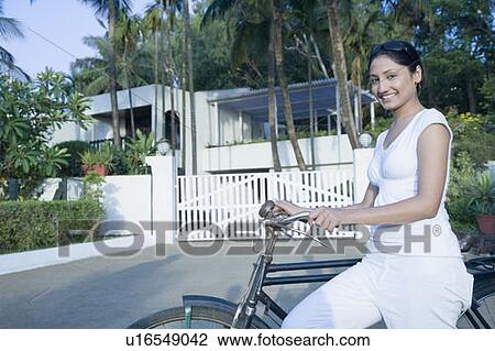 Portrait of a young woman standing with a bicycle in front of a house View Large Photo Image Stock Image - Portrait of a young woman standing with a bicycle in front of a house. Fotosearch