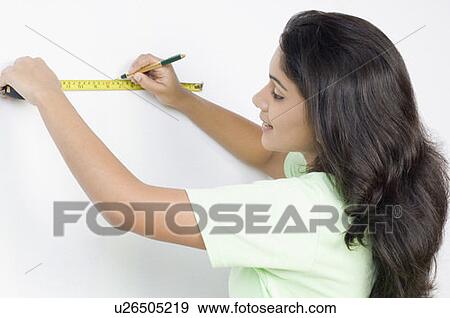 Stock Photo - Side profile of a young woman measuring a wall with a tape measure. Fotosearch