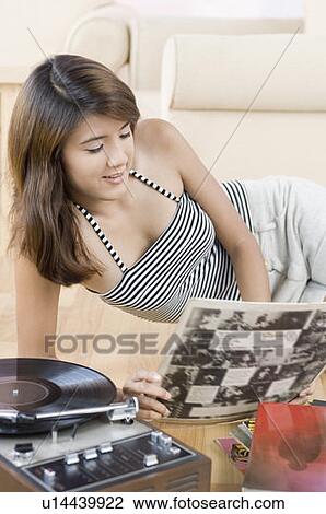 Stock Image - Young woman listening to music and looking at a photo album. Fotosearch